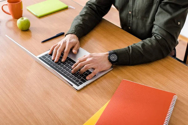 Cropped view of male student using laptop at desk with notebooks — Stock Photo