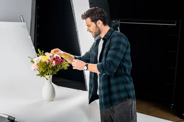 Giovane fotografo sorridente che organizza fiori in studio fotografico — Foto stock