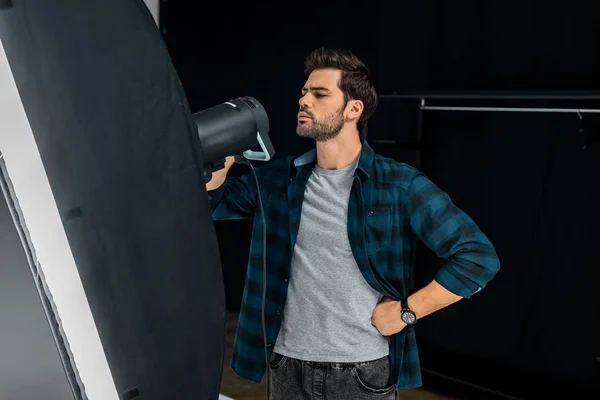 Bel giovane uomo che lavora con attrezzature di illuminazione in studio fotografico — Foto stock