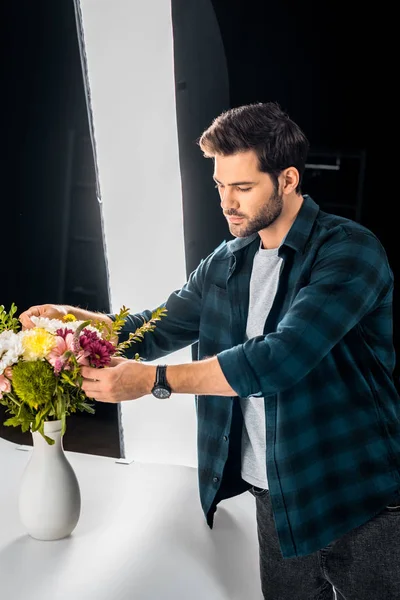 Schöner junger Mann arrangiert Blumen in professionellem Fotostudio — Stockfoto