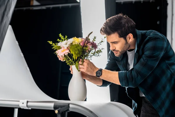 Bonito jovem fotógrafo arranjar flores no estúdio de fotos — Fotografia de Stock