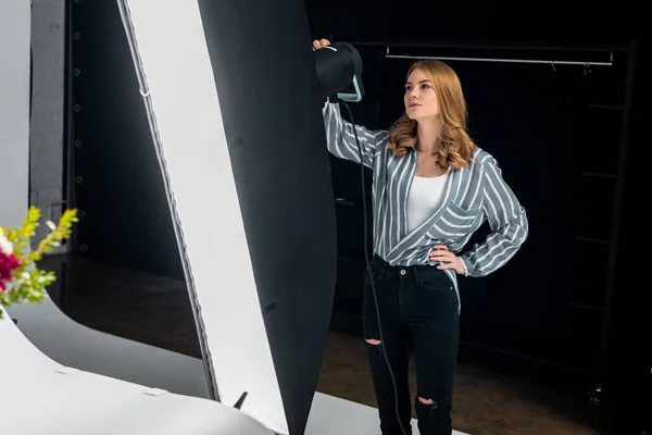 Schöne junge Frau arbeitet mit Beleuchtungstechnik im Fotostudio — Stockfoto