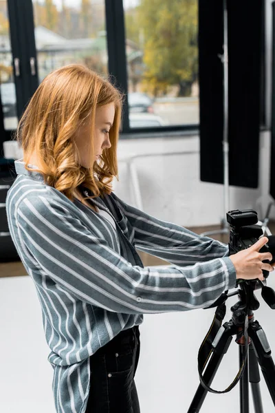 Side view of beautiful young woman photographing with camera in photo studio — Stock Photo