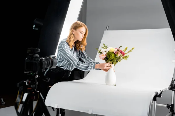 Vista ravvicinata della macchina fotografica e giovane donna che organizza fiori in studio fotografico — Foto stock