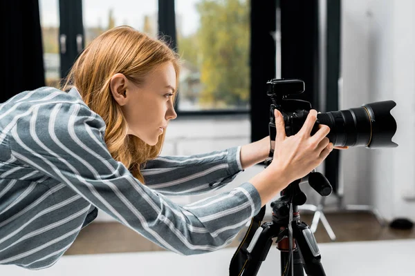 Vista lateral de una joven fotógrafa trabajando con una cámara fotográfica profesional en un estudio - foto de stock