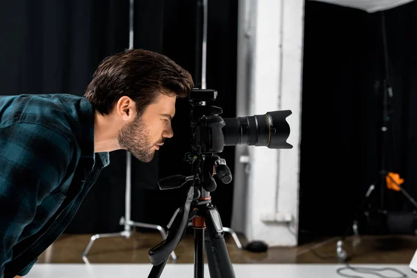 Vista lateral del joven fotógrafo trabajando con una cámara fotográfica profesional en el estudio - foto de stock