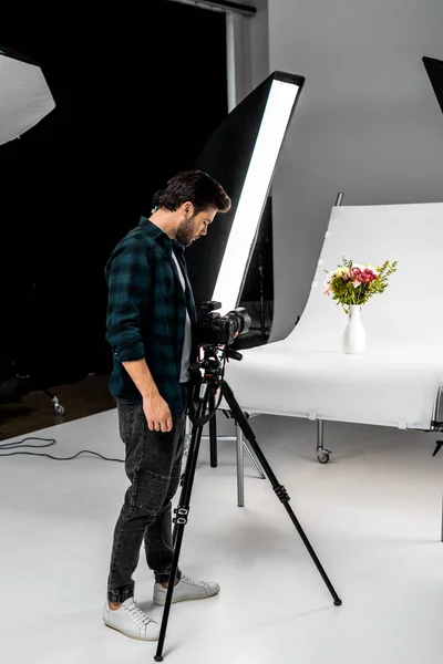 Handsome young photographer shooting beautiful flowers in professional photo studio — Stock Photo