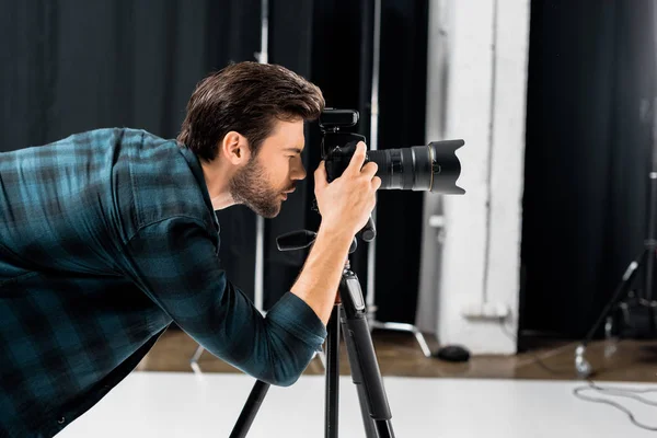 Vista lateral del joven fotógrafo profesional que trabaja con la cámara en el estudio de fotografía - foto de stock