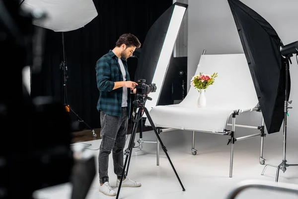 Jovem fotógrafo profissional que trabalha com câmera e equipamentos de iluminação no estúdio de fotografia — Fotografia de Stock