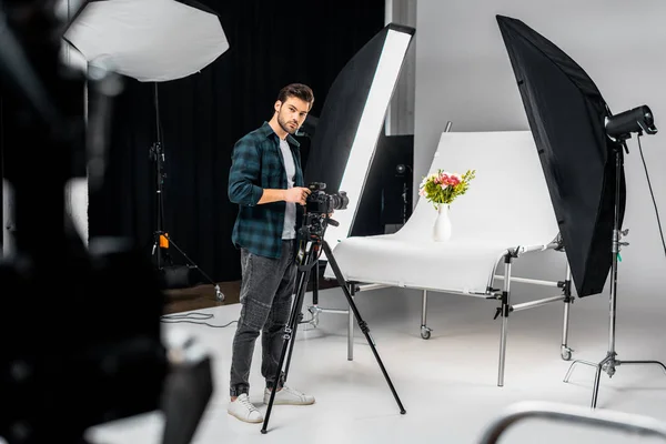 Bonito jovem fotógrafo trabalhando com câmera e equipamentos de iluminação no estúdio de fotografia — Fotografia de Stock