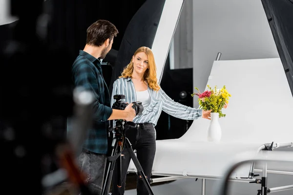 Selective focus of young photographers looking at each other while shooting flowers in studio — Stock Photo