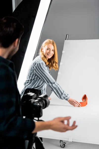 Cropped shot of male photographer looking at colleague arranging shoe in studio — Stock Photo