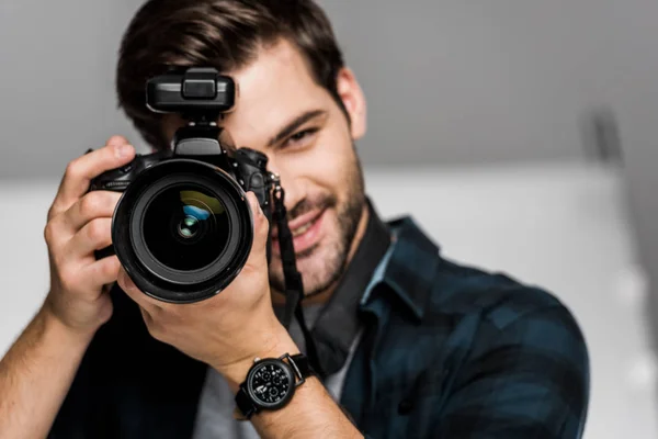Giovane uomo sorridente che fotografa con macchina fotografica in studio — Foto stock