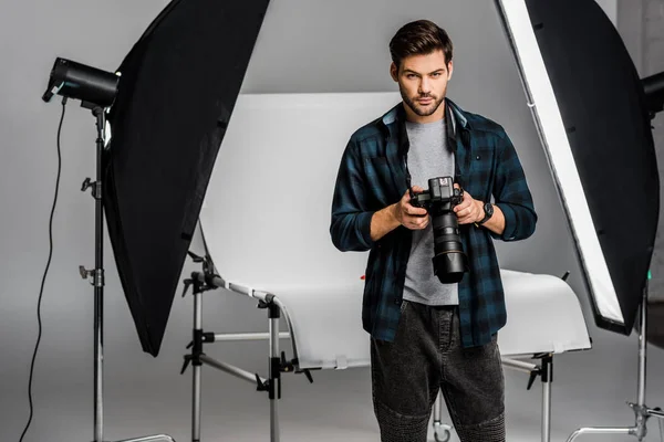 Handsome professional young photographer using camera in photo studio — Stock Photo