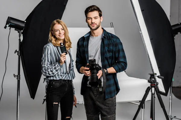 Jóvenes fotógrafos con equipo profesional de pie juntos y sonriendo a la cámara en el estudio de fotografía - foto de stock