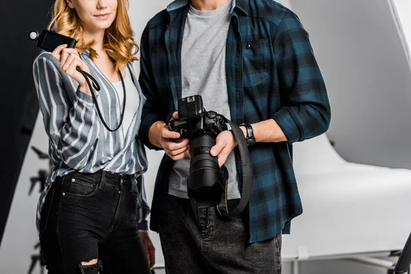 Cropped shot of young photographers holding camera and light meter in studio — Stock Photo