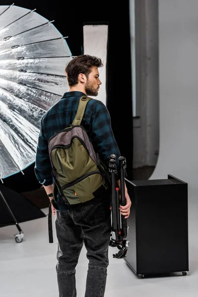 Back view of young man with backpack holding professional equipment in photo studio — Stock Photo