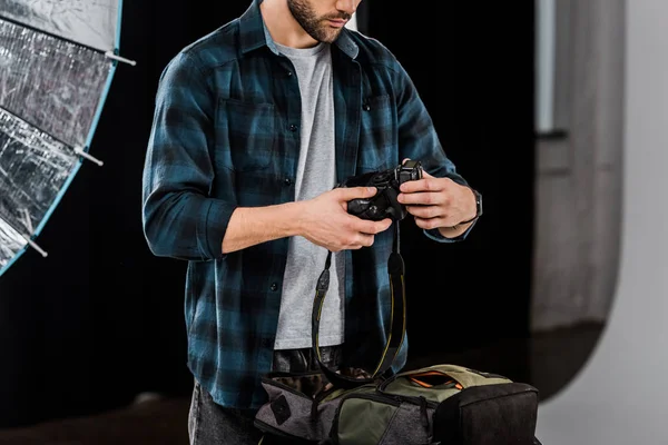 Cropped shot of professional young photographer packing camera in backpack in photo studio — Stock Photo