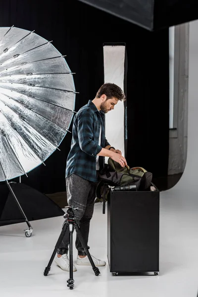 Vista laterale del giovane fotografo professionista che impacchetta la fotocamera nello zaino in studio fotografico — Foto stock