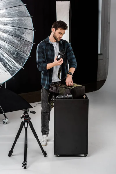 Fotógrafo joven profesional embalaje de la cámara en la mochila en el estudio de fotos - foto de stock