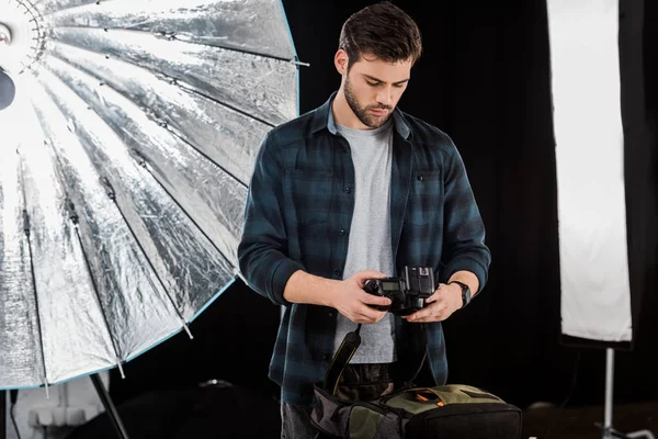 Bonito jovem fotógrafo câmera de embalagem na mochila no estúdio de fotos — Fotografia de Stock