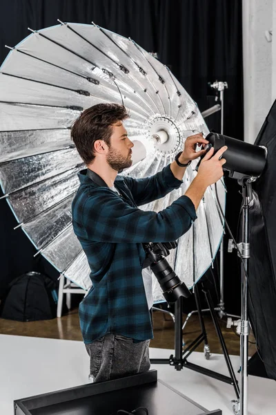 Beau jeune photographe travaillant avec un équipement d'éclairage professionnel dans un studio photo — Photo de stock