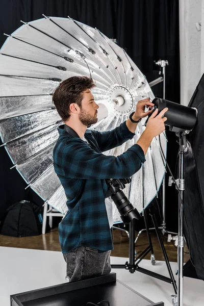 Joven fotógrafo guapo trabajando con equipo de iluminación profesional en estudio fotográfico - foto de stock