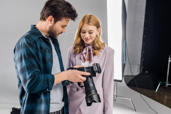 Bonito jovem fotógrafo e sorridente fêmea modelo usando foto câmera juntos no estúdio — Fotografia de Stock