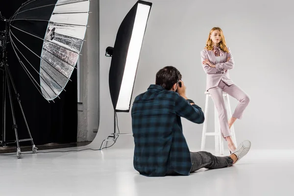 Rückseite des Fotografen sitzt und fotografiert schöne weibliche Modell im Studio — Stockfoto