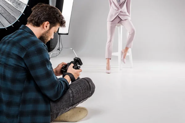 Photographe assis avec appareil photo et jeune mannequin posant en studio photo — Photo de stock