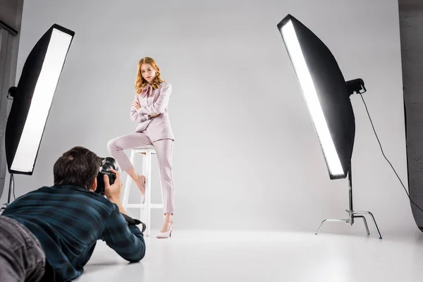 Jovem fotógrafo com câmera deitada e fotografando belo modelo feminino posando em estúdio — Fotografia de Stock