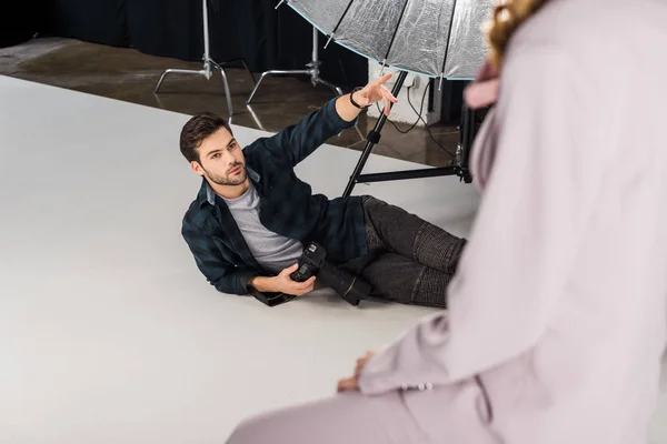 Високий кут зору фотографа з камерою, що лежить і пояснює роботу жіночій моделі в студії — стокове фото