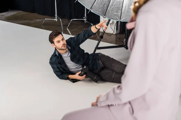 Vue grand angle du photographe avec caméra couché et expliquant le travail au modèle féminin en studio — Photo de stock