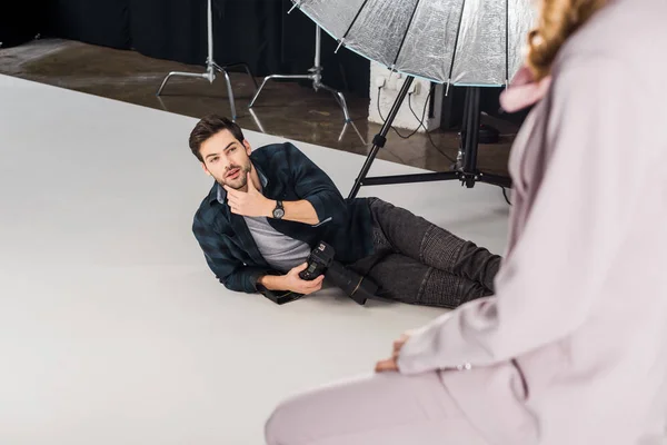 Vue grand angle du photographe avec appareil photo couché et travaillant avec modèle féminin en studio — Photo de stock