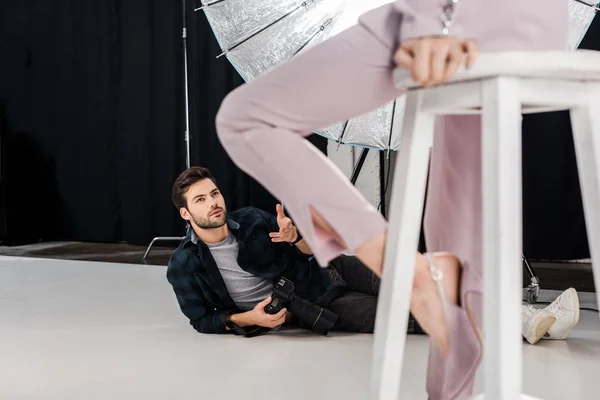 Plan recadré d'un photographe couché avec un appareil photo et travaillant avec un mannequin en studio photo — Photo de stock