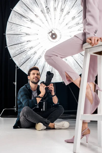 Tiro recortado de fotógrafo sorrindo sentado e fotografando modelo elegante em estúdio — Fotografia de Stock