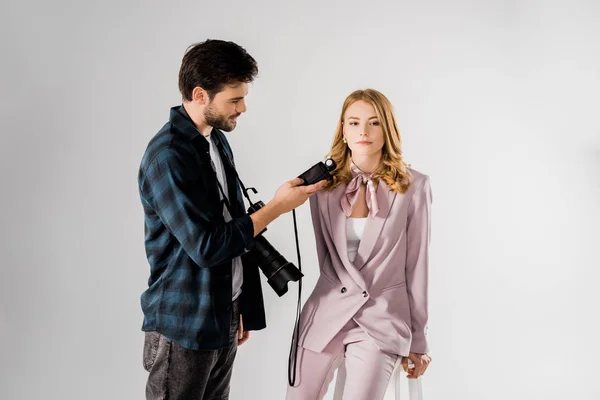 Giovane fotografo sorridente usando il misuratore di luce e lavorando con un bellissimo modello in studio — Foto stock