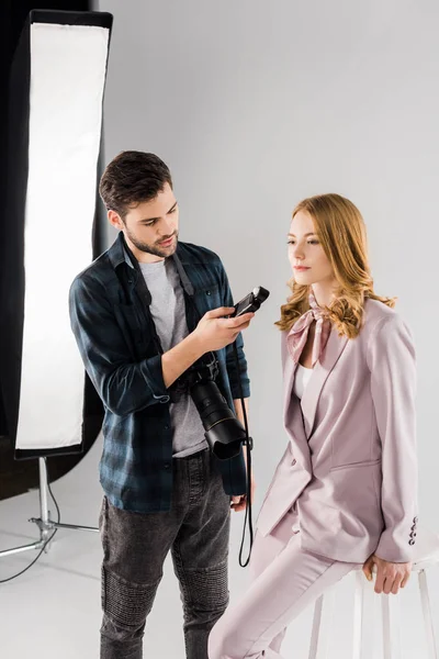 Young photographer holding light meter and working with female model in photo studio — Stock Photo