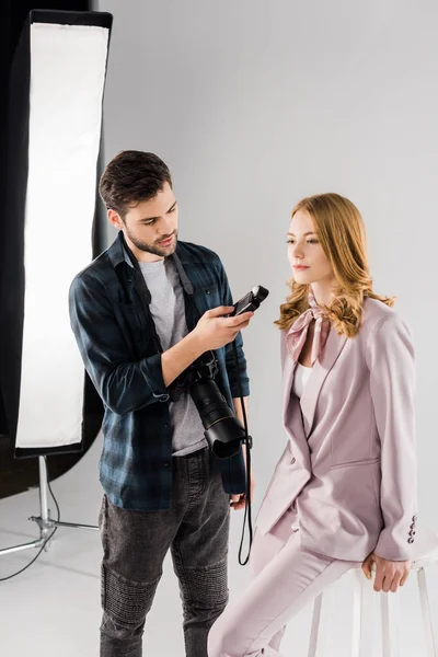 Jovem fotógrafo segurando medidor de luz e trabalhando com modelo feminino no estúdio de fotografia — Fotografia de Stock