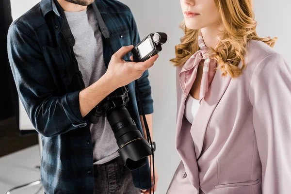 Cropped shot of young photographer holding light meter and working with female model in studio — Stock Photo