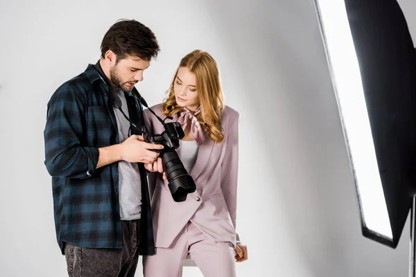 Fotógrafo masculino e bela jovem verificando fotos na câmera no estúdio de fotos — Fotografia de Stock