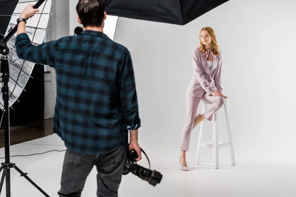 Visão traseira do fotógrafo segurando câmera e modelo posando em estúdio — Fotografia de Stock