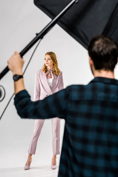 Visão traseira do fotógrafo trabalhando com equipamentos de iluminação enquanto modelo feminino posando em estúdio — Fotografia de Stock