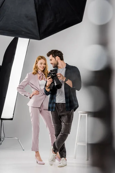 Selective focus of smiling young photographer and model checking photos on camera in studio — Stock Photo