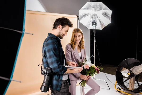 Sorrindo jovem fotógrafo mostrando laptop para bela modelo feminina no estúdio de fotos — Fotografia de Stock