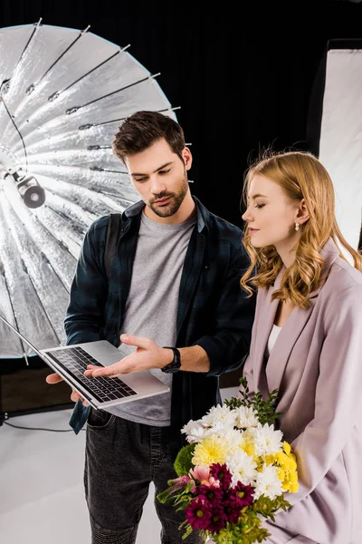 Young photographer showing laptop to beautiful female model in photo studio — Stock Photo