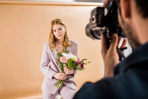 Scatto ritagliato di fotografo ripresa bella giovane modello femminile con mazzo di fiori in studio — Foto stock