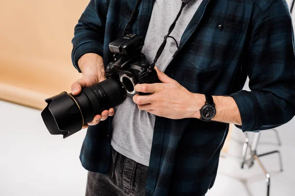 Sección media de joven fotógrafo sosteniendo cámara fotográfica profesional en el estudio - foto de stock