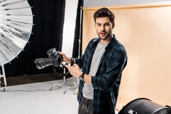 Surprised young photographer pointing at camera in photo studio — Stock Photo