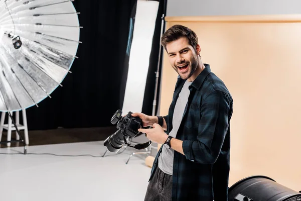 Cheerful young photographer pointing at photo camera in studio — Stock Photo